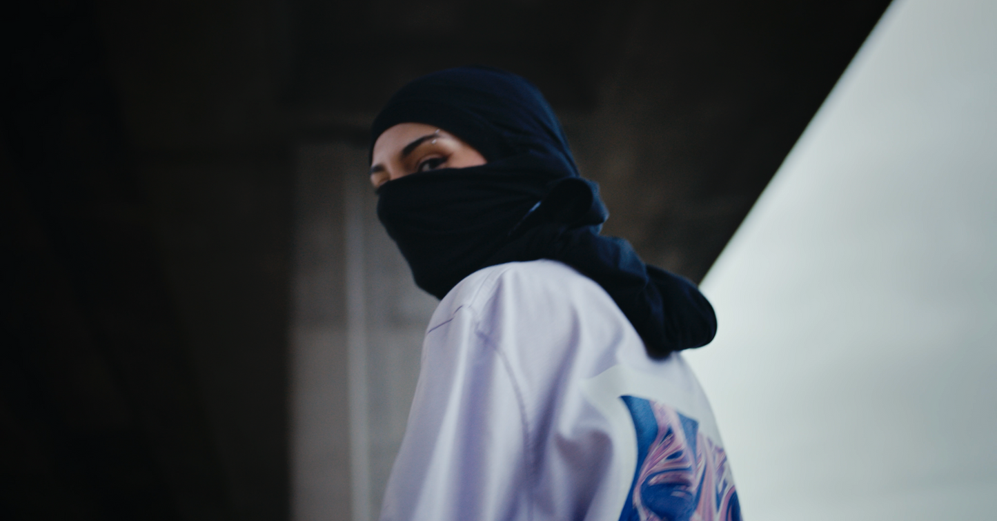 closeup violet oversized VOODOO PASTELLE longsleeve tee on 165cm female model wearing baclava in trainyard background
