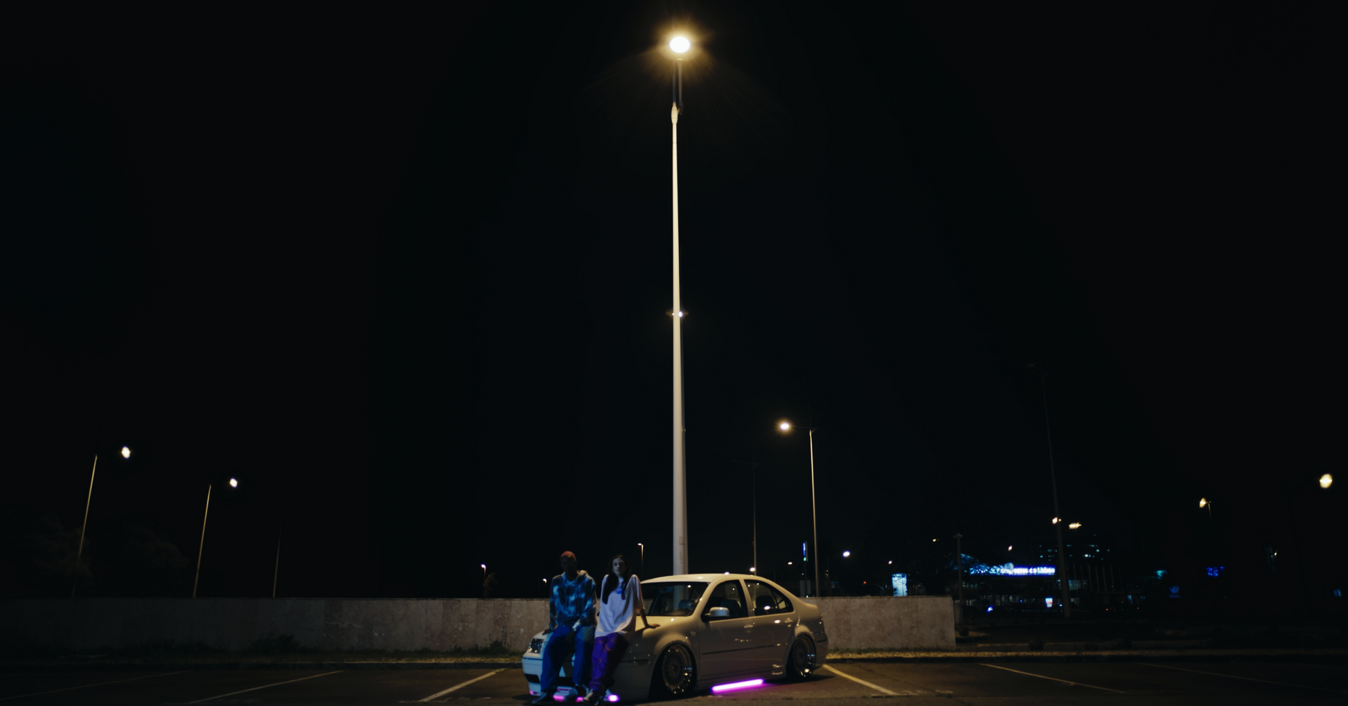 long distance night shot of salmon coloured daydreaming box fit oversized PASTELLE tee on female 165cm model alongside male 185cm model wearing a PASTELLE hoodie