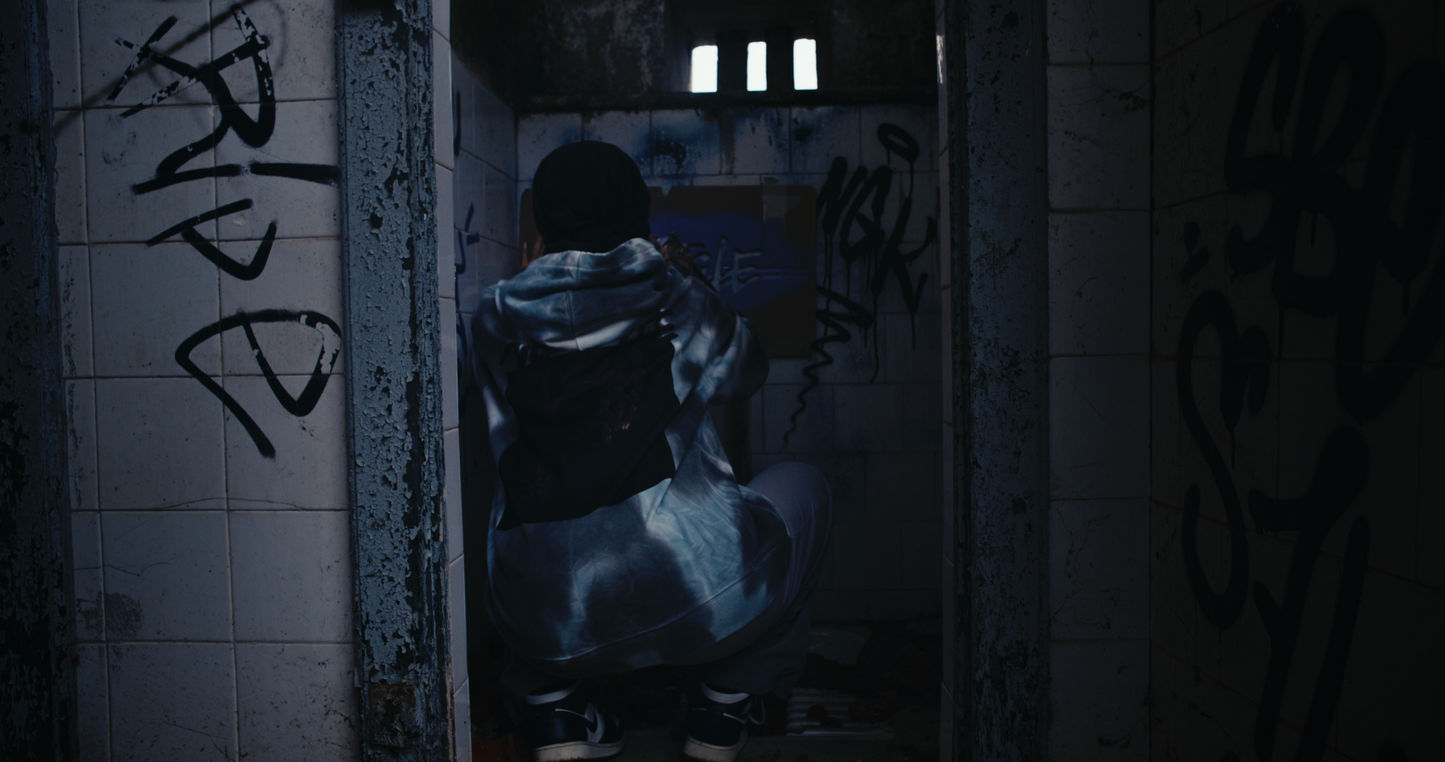 female model wearing PASTELLE hoodie spraying grafitti of pastelle logo on bathroom wall