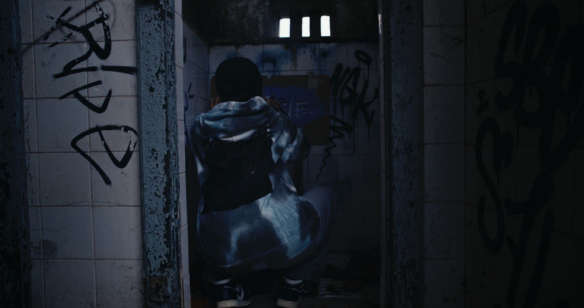 female model wearing PASTELLE hoodie spraying grafitti of pastelle logo on bathroom wall