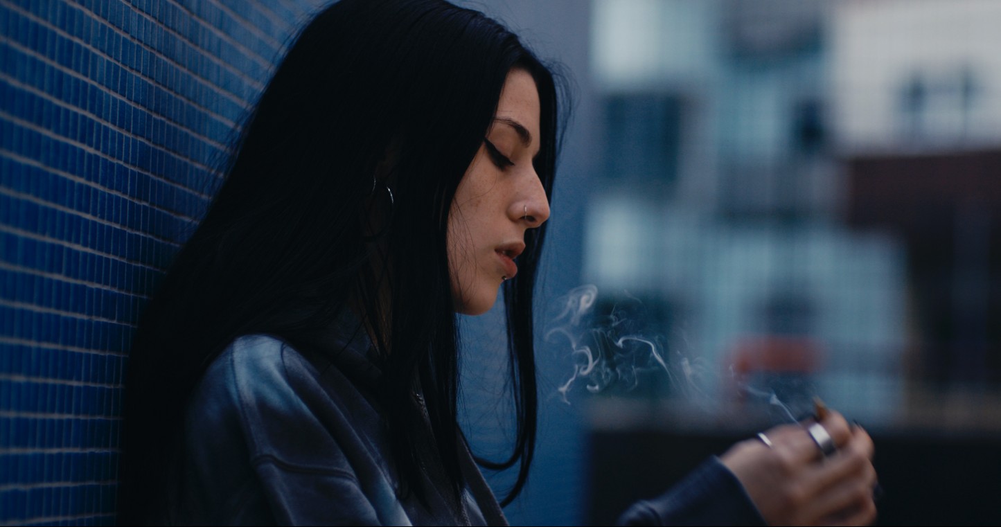closeup shot of female model with dark hair smoking against blue backdrop wearing PASTELLE hoodie